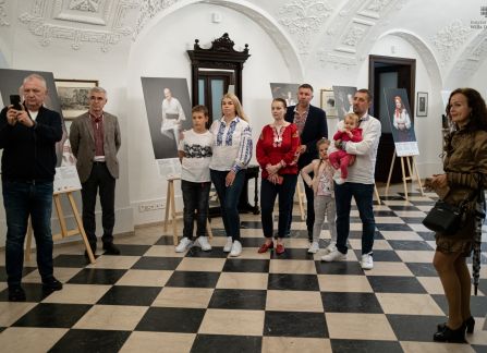 Fotografia. wernisaż wystawy piękno jedności w willi decjusza. w Holu głównym pod ścianami na sztalugach stoją fotografie. na środku stoją Goście wernisażu.